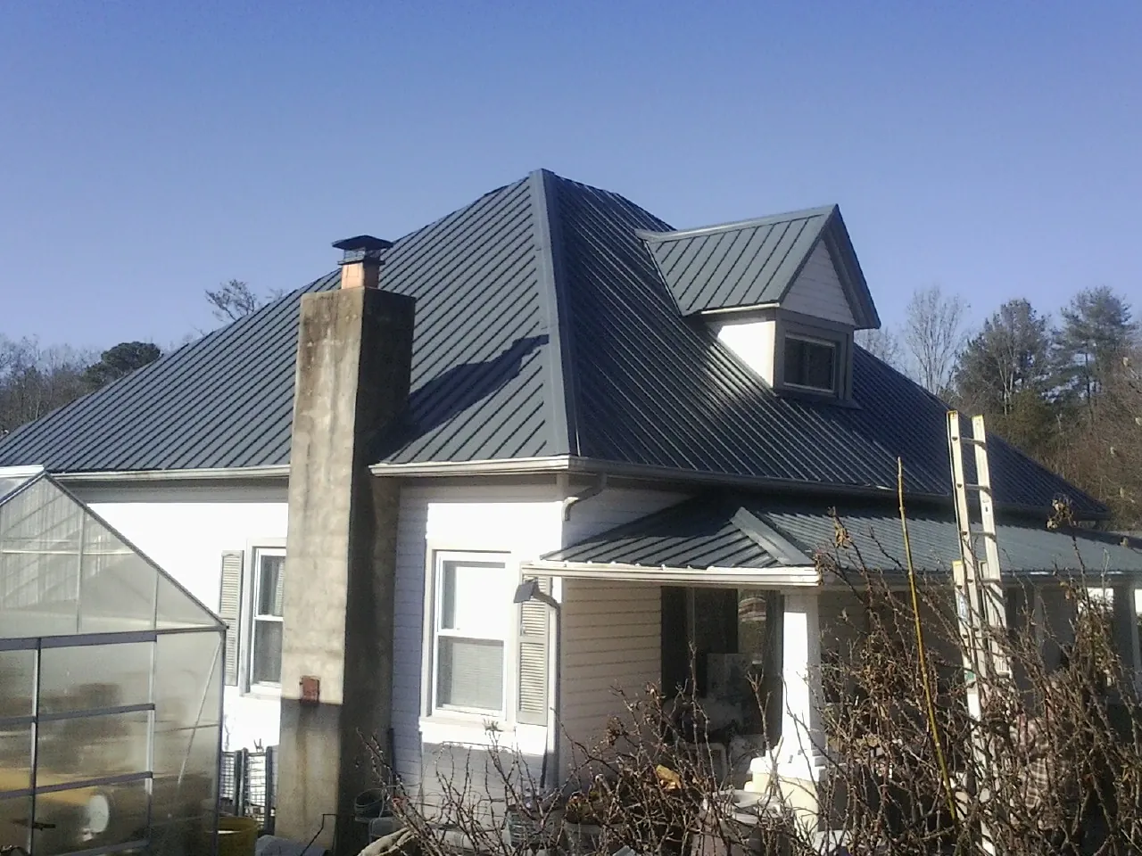 Dark blue standing seam metal roof on a white farmhouse with dormer — Slate & Tile Roof Repair by Roofing Brothers in East Otis
