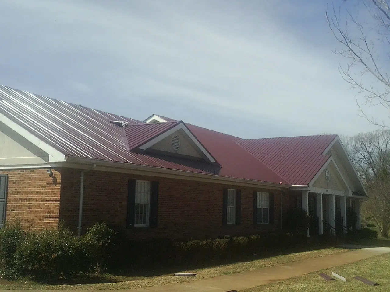 Red metal roof with gabled entries on a long brick building, from a Hail Damage Roof Repair job in East Otis