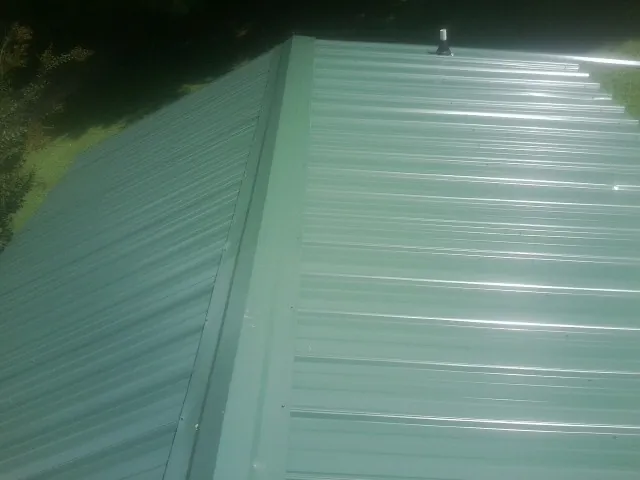 New green metal panels meeting at the ridge of a roof — Flat Roof Repair work by our crew in East Otis