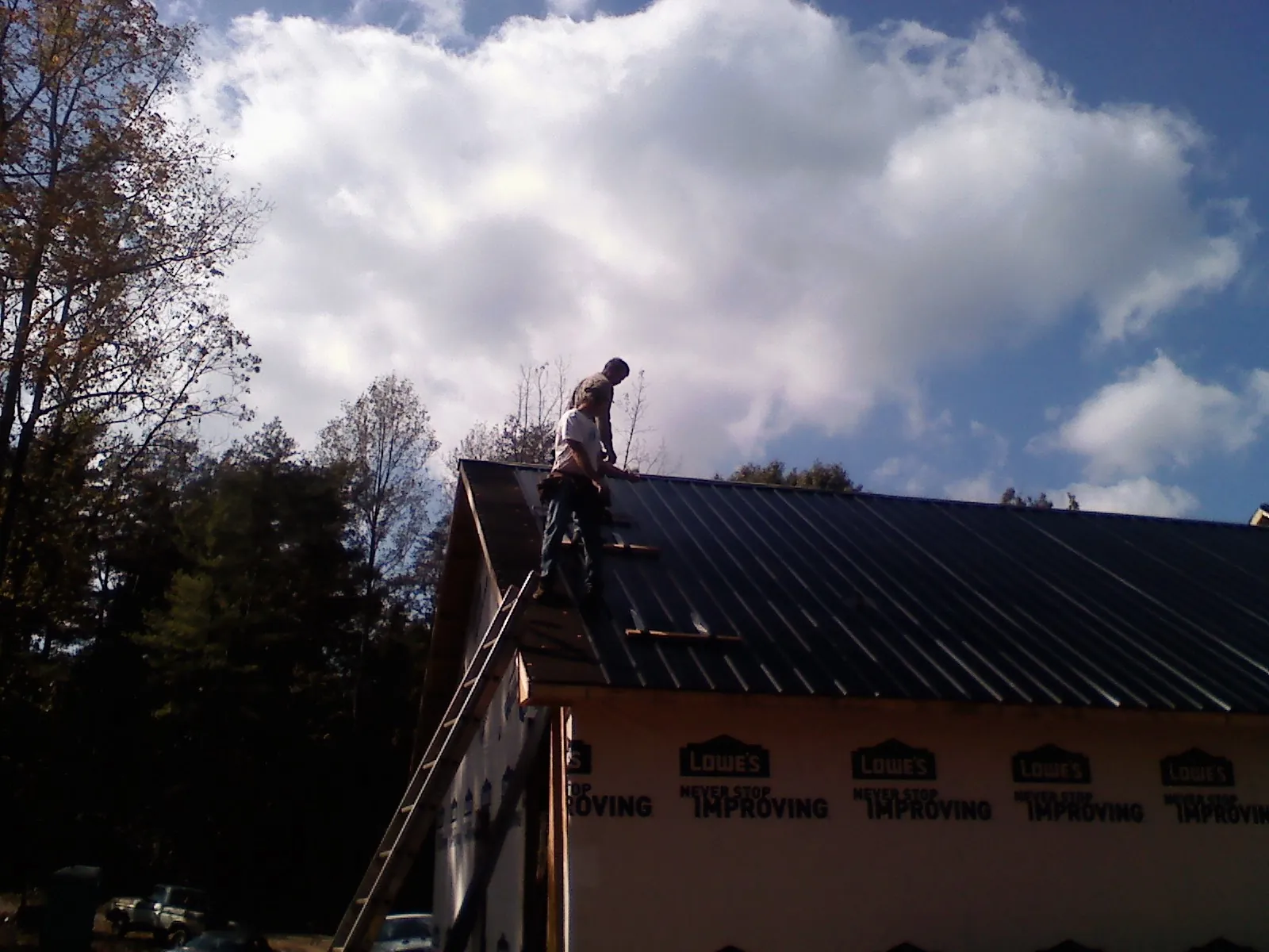 Roofer fastening dark metal panels high against a cloudy sky, from a Roof Inspection job in East Otis