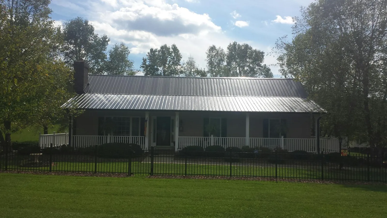 Gray metal roof on a brick ranch with a full width front porch — Gutter Guard Installation work by our crew in East Otis