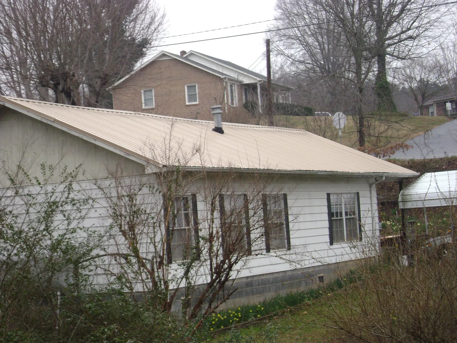 Tan metal roof on a white sided house set into a hillside — Commercial Roofing by Roofing Brothers in East Otis