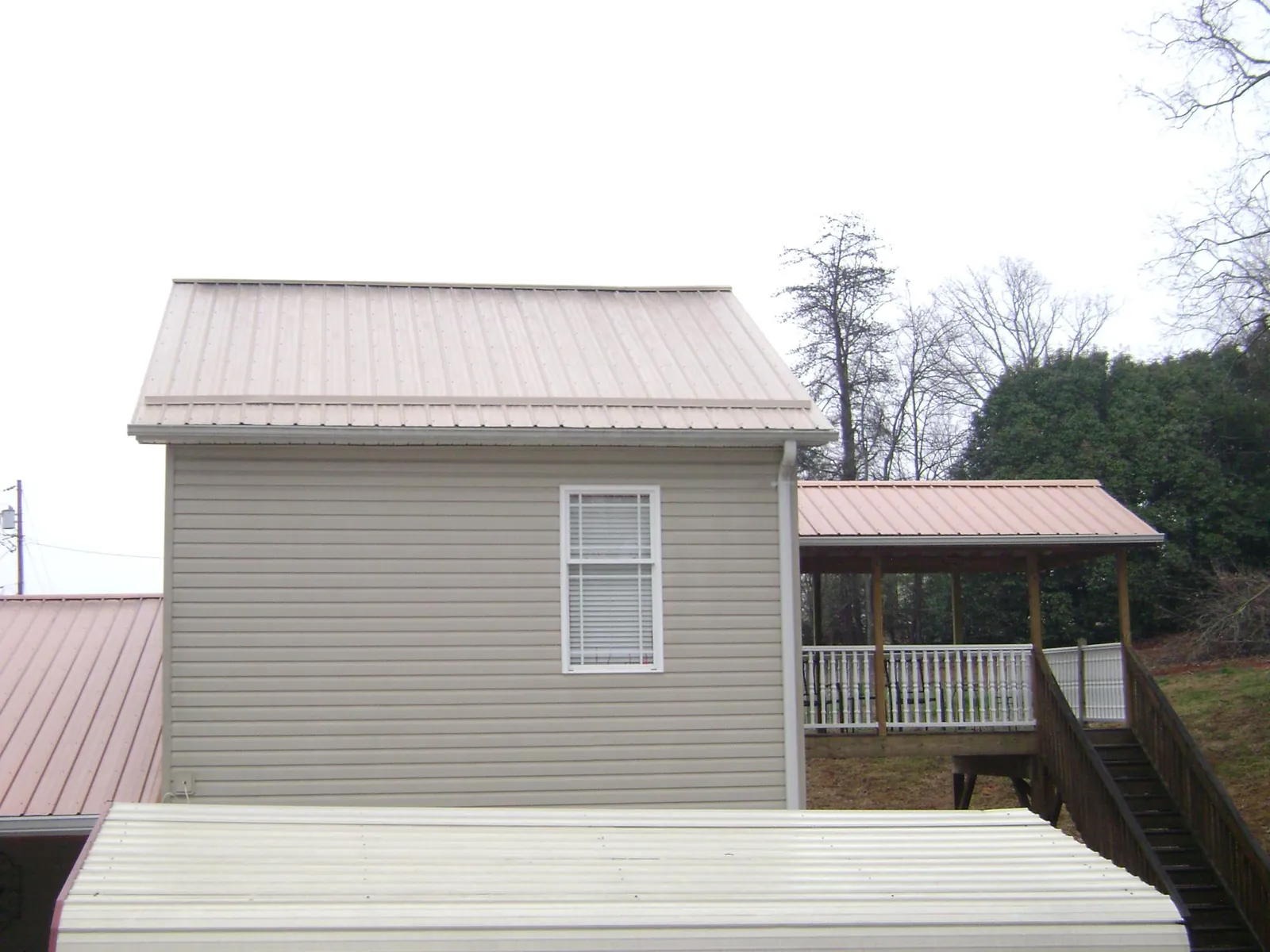 Tan metal roofs on a two story addition and attached porch, from a Roof Replacement job in East Otis